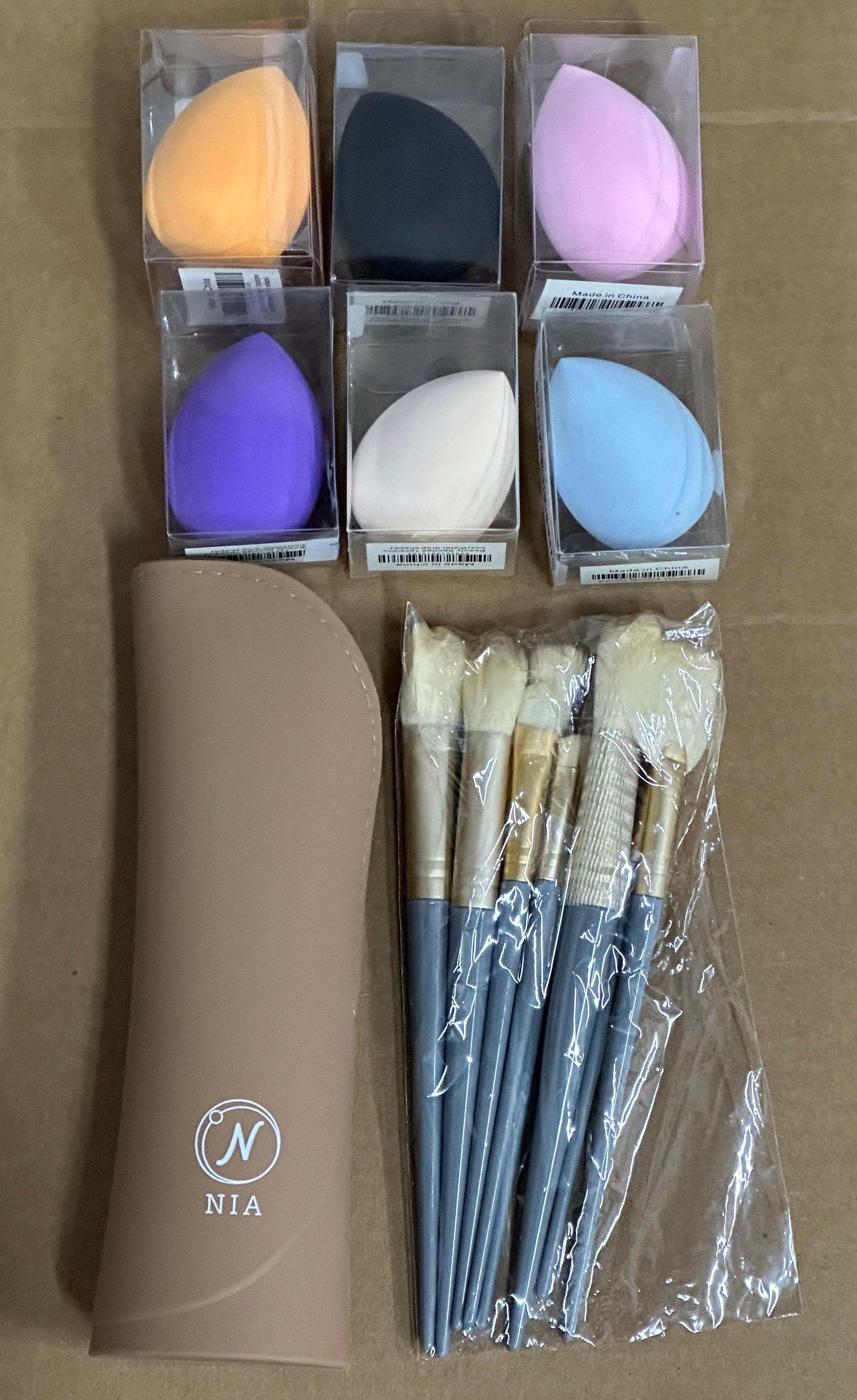 Set of makeup brushes and sponges with a NIA branded case on a cardboard background
